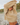 A woman outdoors on a rocky beach wearing a chunky knit beige sweater with her arms over her head and her eyes closed in a relaxed pose.