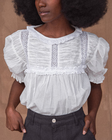A woman wearing a white, vintage-inspired blouse with billowy sleeves and lace detailing on the yoke, tucked into dark pants.