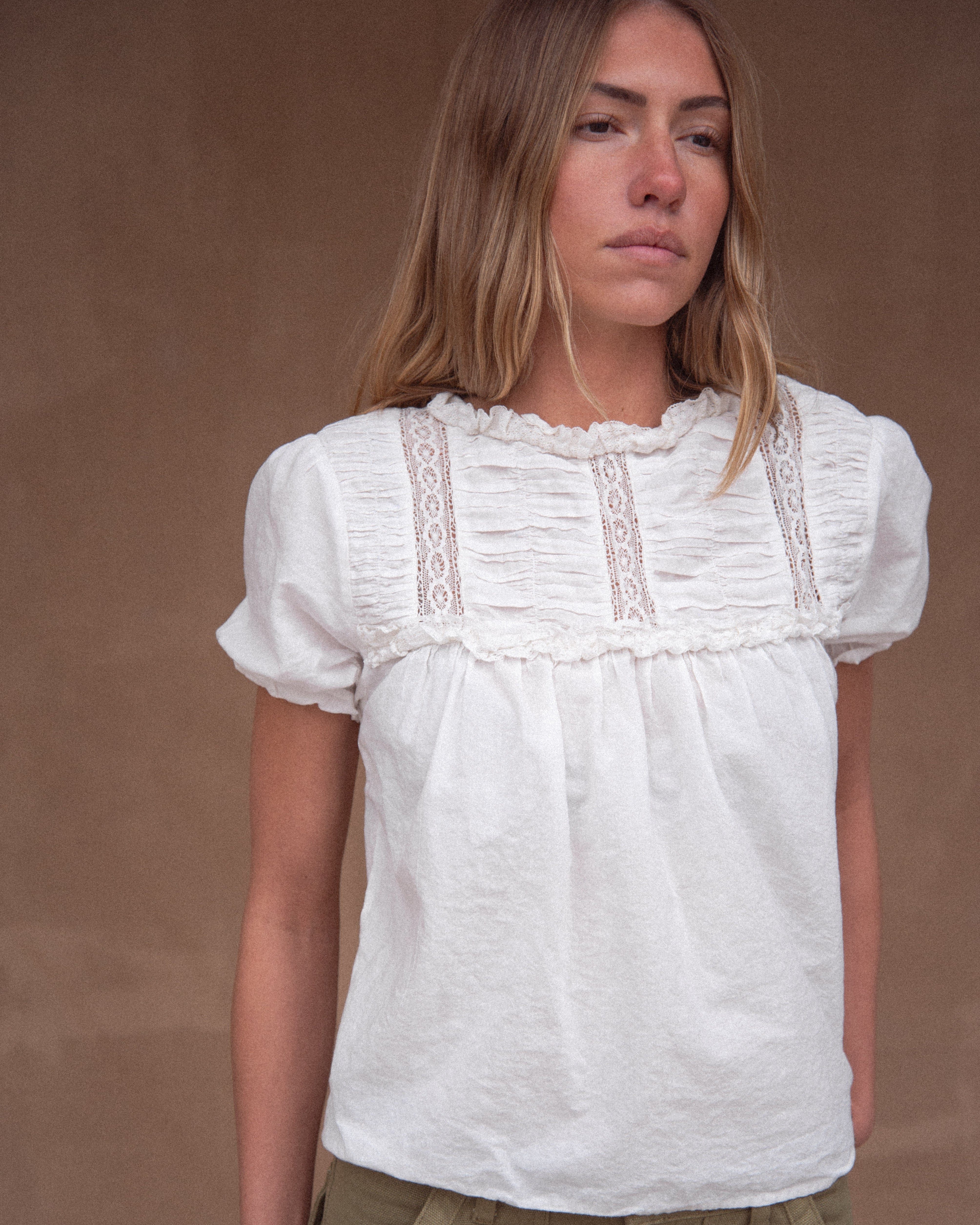 A woman wearing a vintage-inspired white blouse with short, billowy sleeves and a flowy bodice, detailed with delicate embroidery and lace.