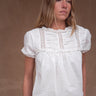 A woman wearing a vintage-inspired white blouse with short, billowy sleeves and a flowy bodice, detailed with delicate embroidery and lace.