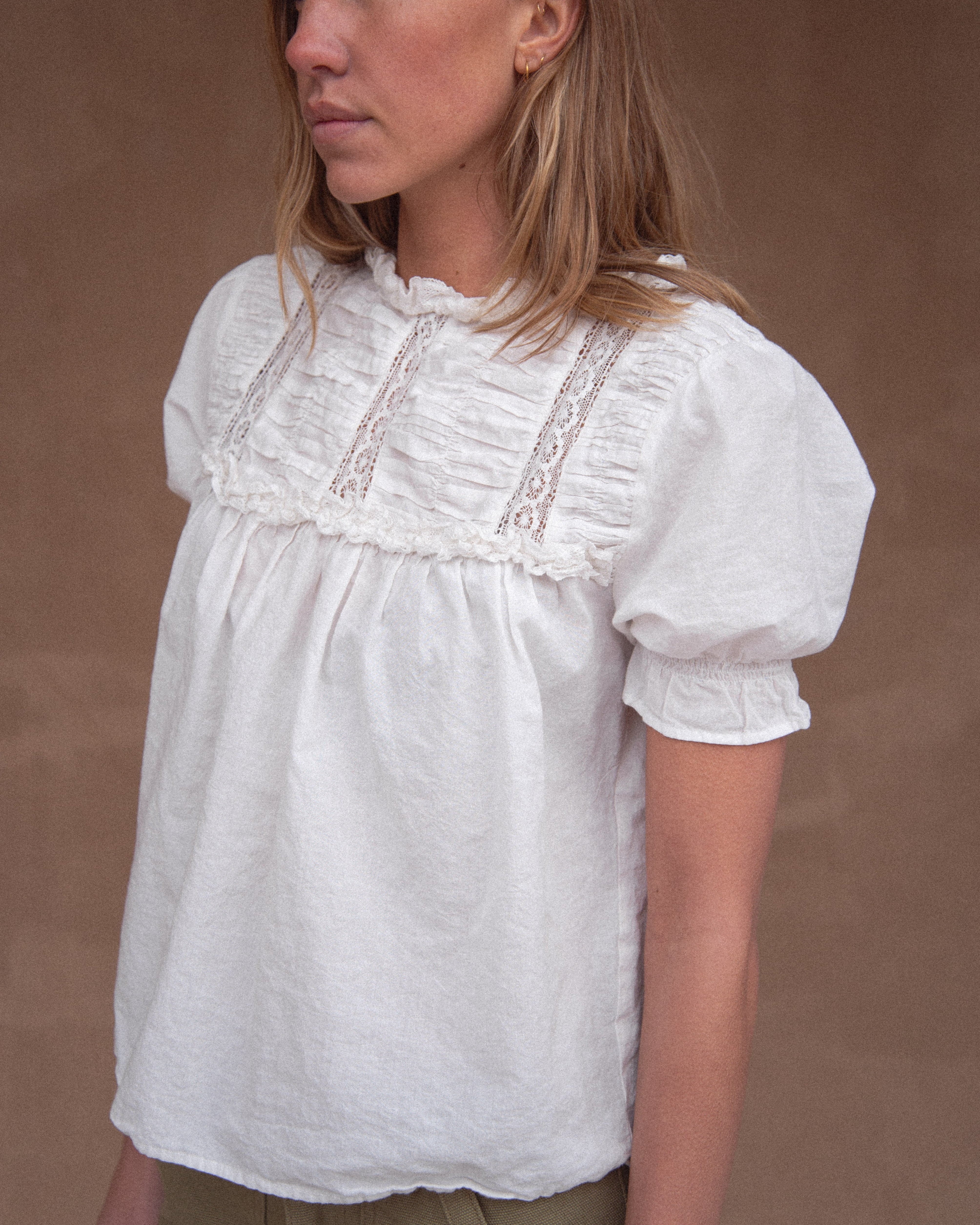 A woman wearing a vintage-inspired white blouse with short, billowy sleeves and a flowy bodice, detailed with delicate embroidery and lace.