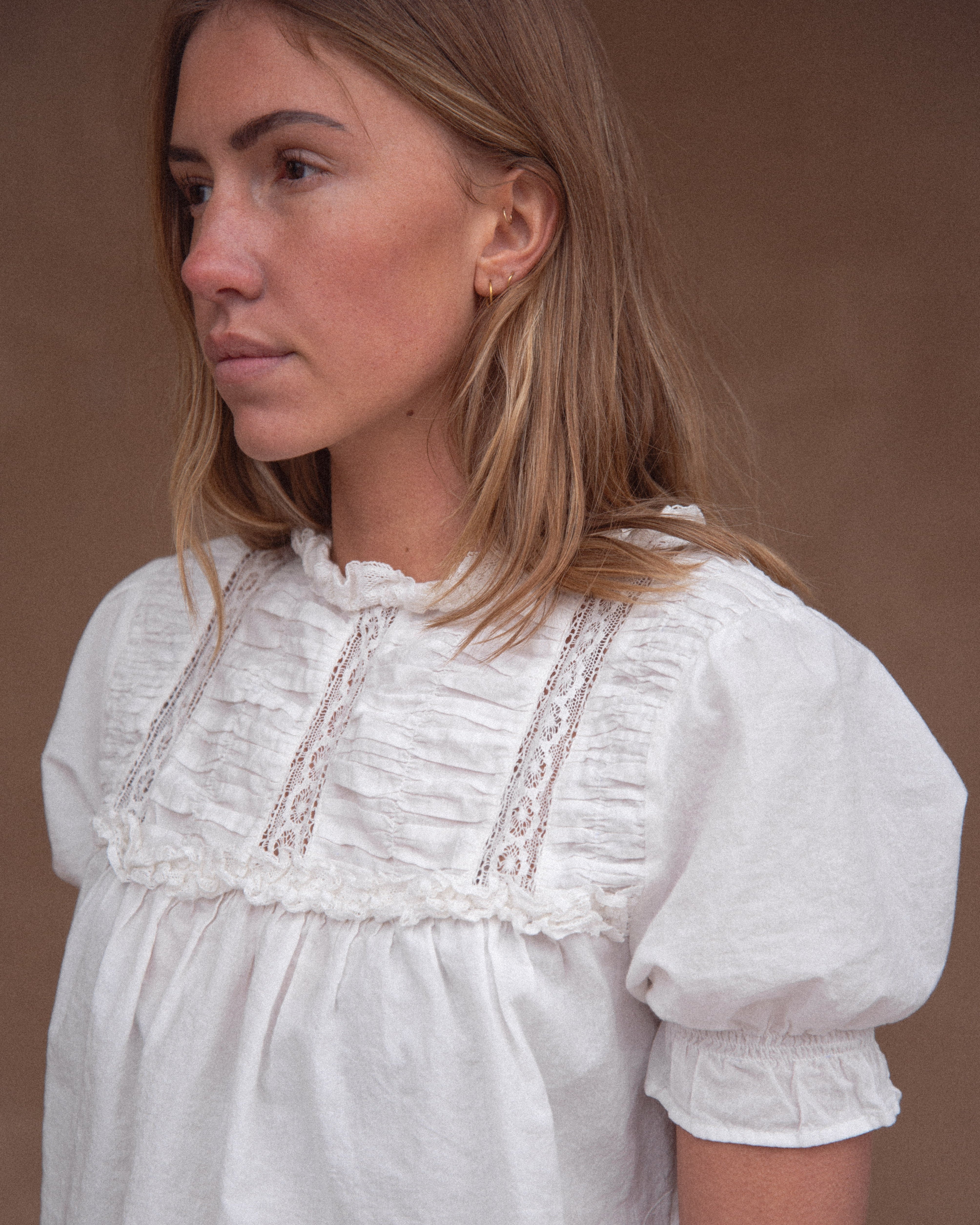 A woman wearing a vintage-inspired white blouse with short, billowy sleeves and a flowy bodice, detailed with delicate embroidery and lace.