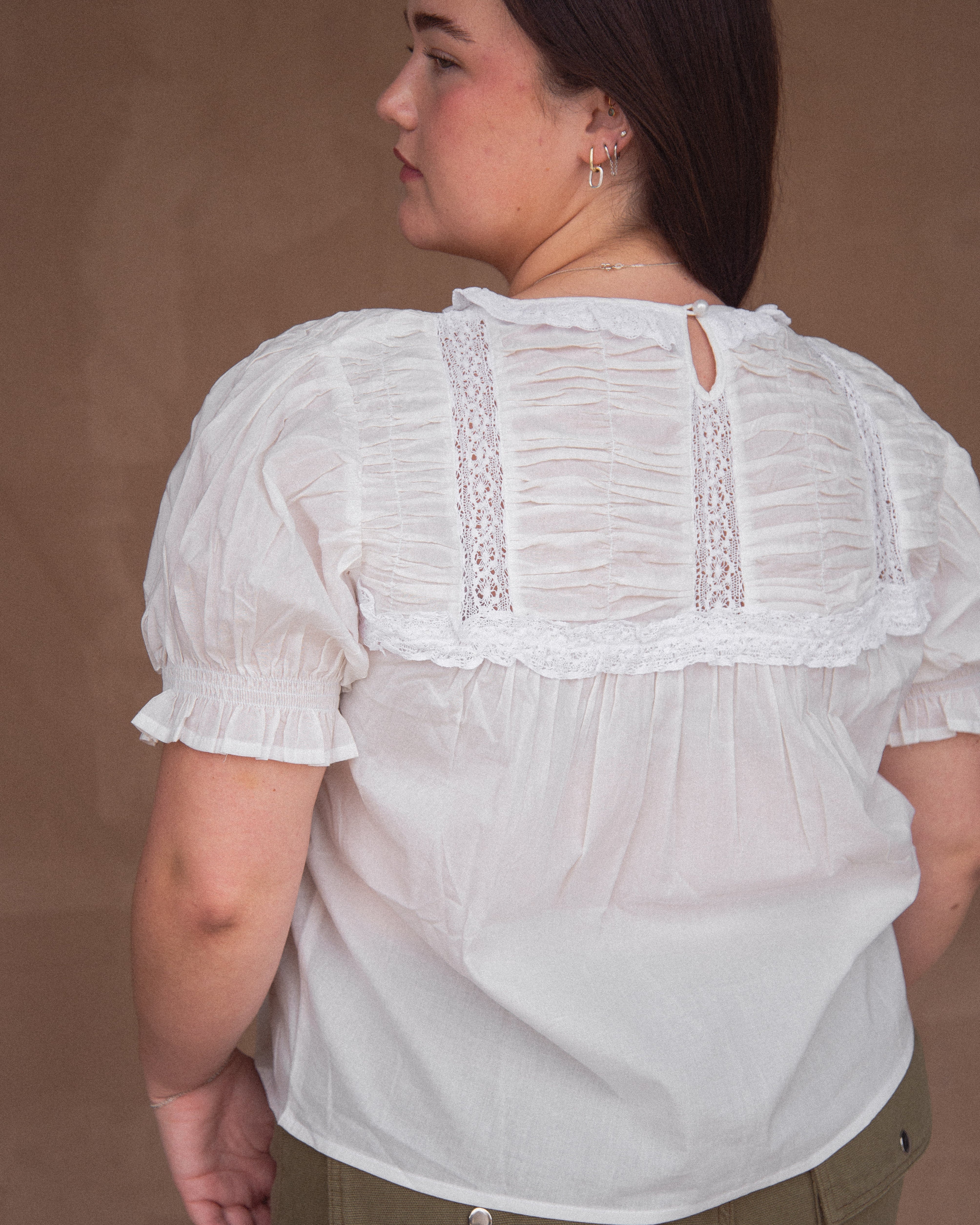 A woman wearing a vintage-inspired white blouse with short, billowy sleeves and a flowy bodice, detailed with delicate embroidery and lace.