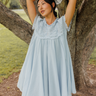Woman in a light blue dress standing next to a tree in a natural setting