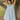 Woman in a light blue dress standing next to a tree in a natural setting