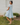 Woman in a light blue dress standing outdoors against a white brick wall.