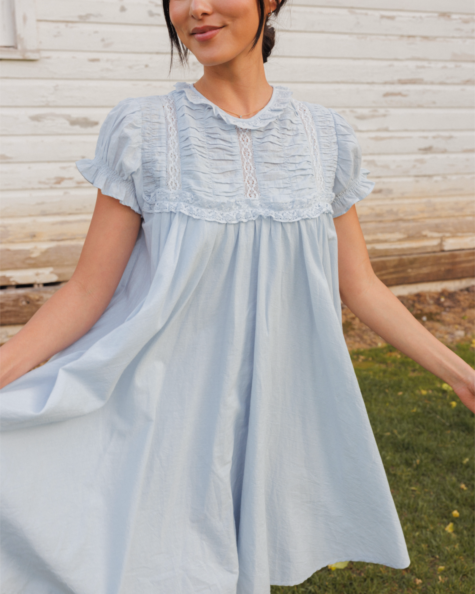 Woman wearing a light blue dress with lace details sitting outdoors.