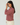 A woman wearing a long-sleeve sweater with thin horizontal burgundy and pink stripes, paired with cream-colored pants, photographed against a plain light gray studio background.