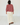 A woman viewed from behind wearing a dusty rose and burgundy striped long-sleeve sweater, cream wide-leg pants, and brown leather loafers, standing in a bright white room with white wooden floorboards.