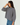 A woman wearing a loose, long-sleeve striped sweater with blue jeans, photographed against a plain light gray studio background.