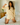 Woman in a yellow loungewear set kneeling on a bed holding a pillow over her head.