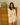Woman wearing a yellow knit outfit standing in front of a wooden dresser.
