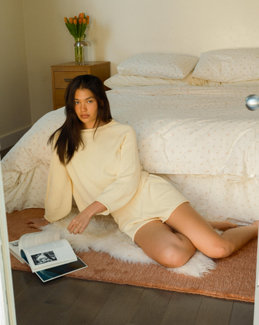 Woman sitting in front of a bed in a bedroom with a open magazine.