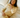 Woman wearing a yellow knit sweater with matching knit shorts on a bed with a floral patterned pillow and sheets.