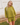 Woman wearing a green knit matching sweater and shorts set standing outdoors with a white wooden structure in the background.