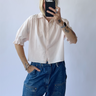 Person wearing a light pink shirt and blue jeans taking a mirror selfie.