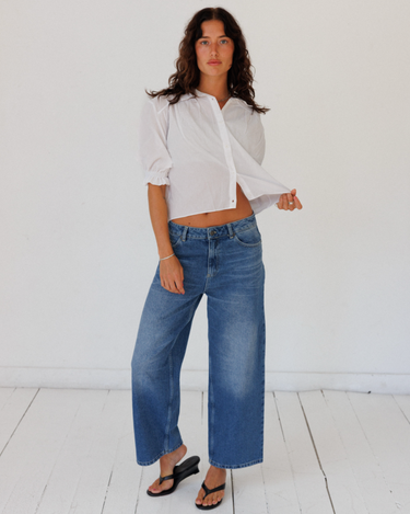 Woman wearing a white blouse and blue jeans against a white background