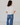 Woman wearing a white blouse and blue jeans against a plain background