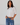 Woman wearing a white blouse and blue jeans against a plain background