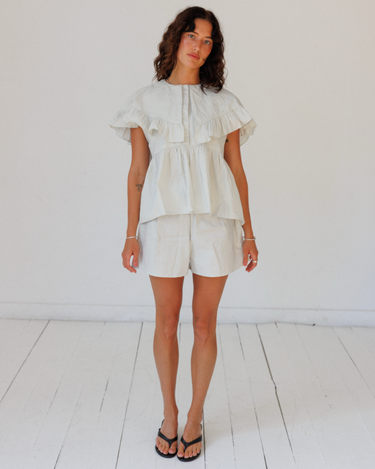 Woman wearing a light-colored blouse and shorts against a white background