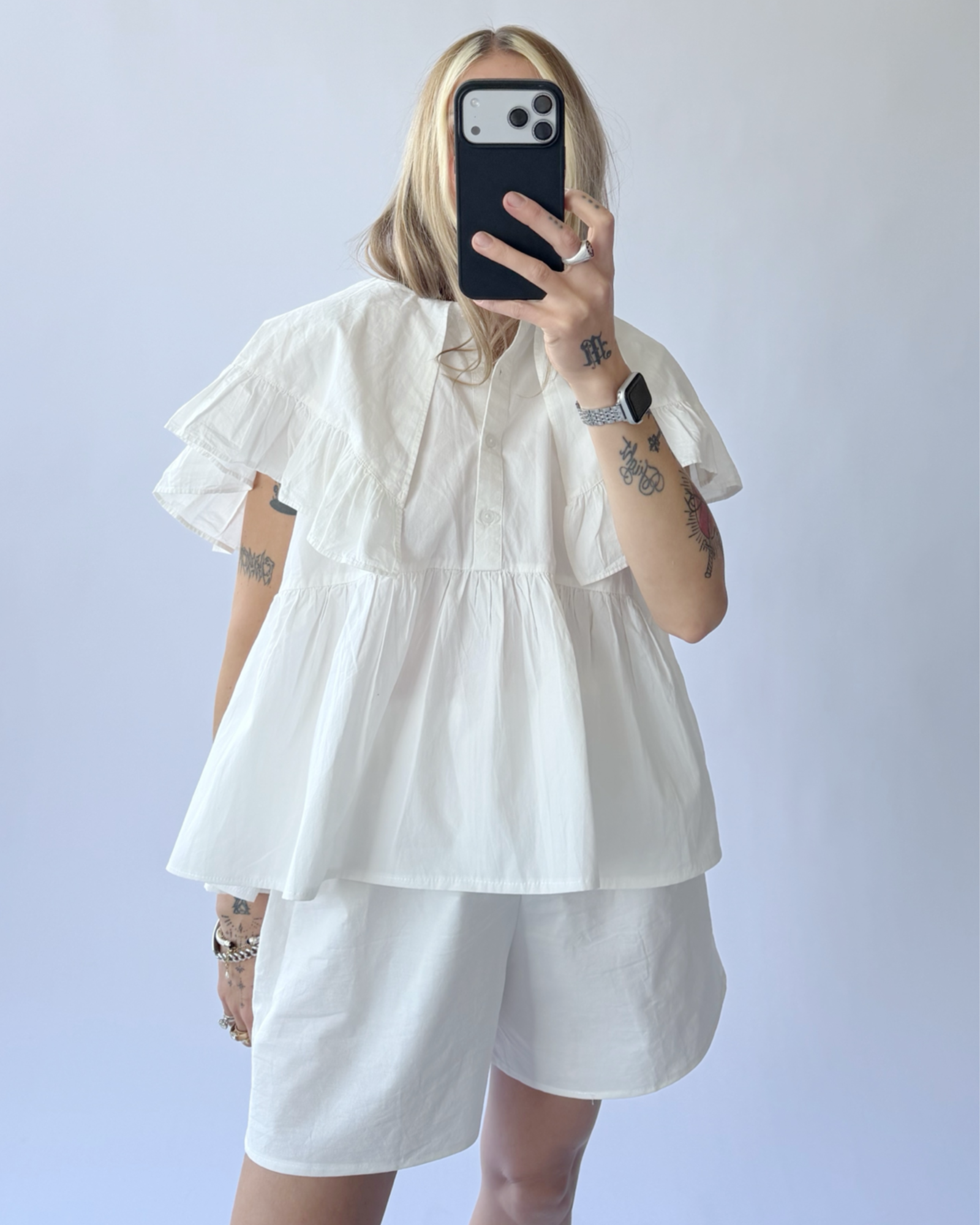 Person wearing a white outfit with ruffled sleeves against a plain background