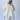 Person wearing a white outfit with ruffled sleeves against a plain background