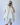 Person wearing a white outfit with ruffled sleeves against a plain background