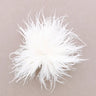 A fluffy white feather pom-pom accessory photographed from above on a plain warm taupe background.