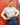 A woman posing in front of a red brick wall, wearing a cream-colored mock neck long-sleeve top and a dark blue pleated skirt.
