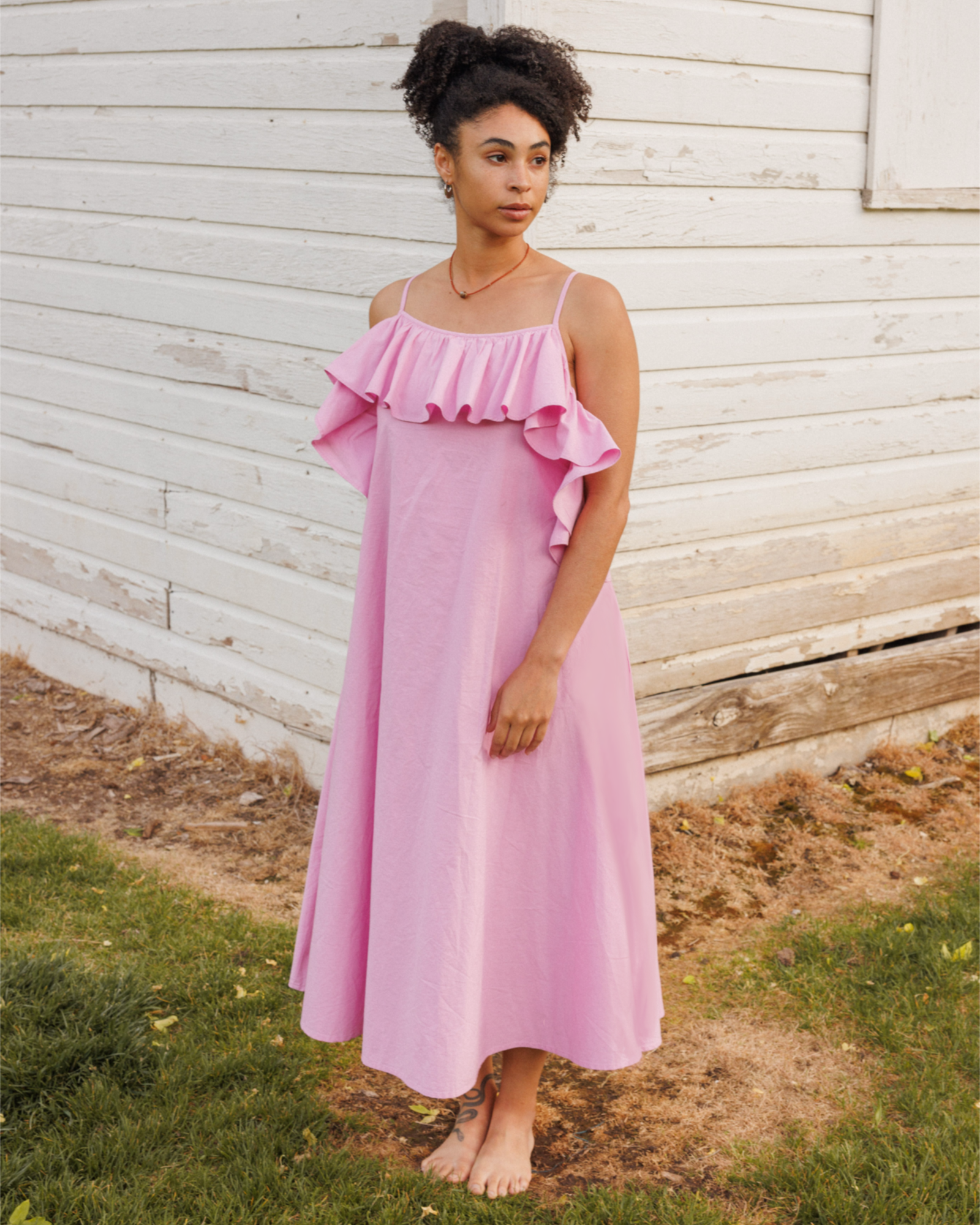 Woman wearing a pink dress standing in front of a wooden wall.