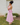 Woman in a pink dress standing outdoors against a white brick wall.