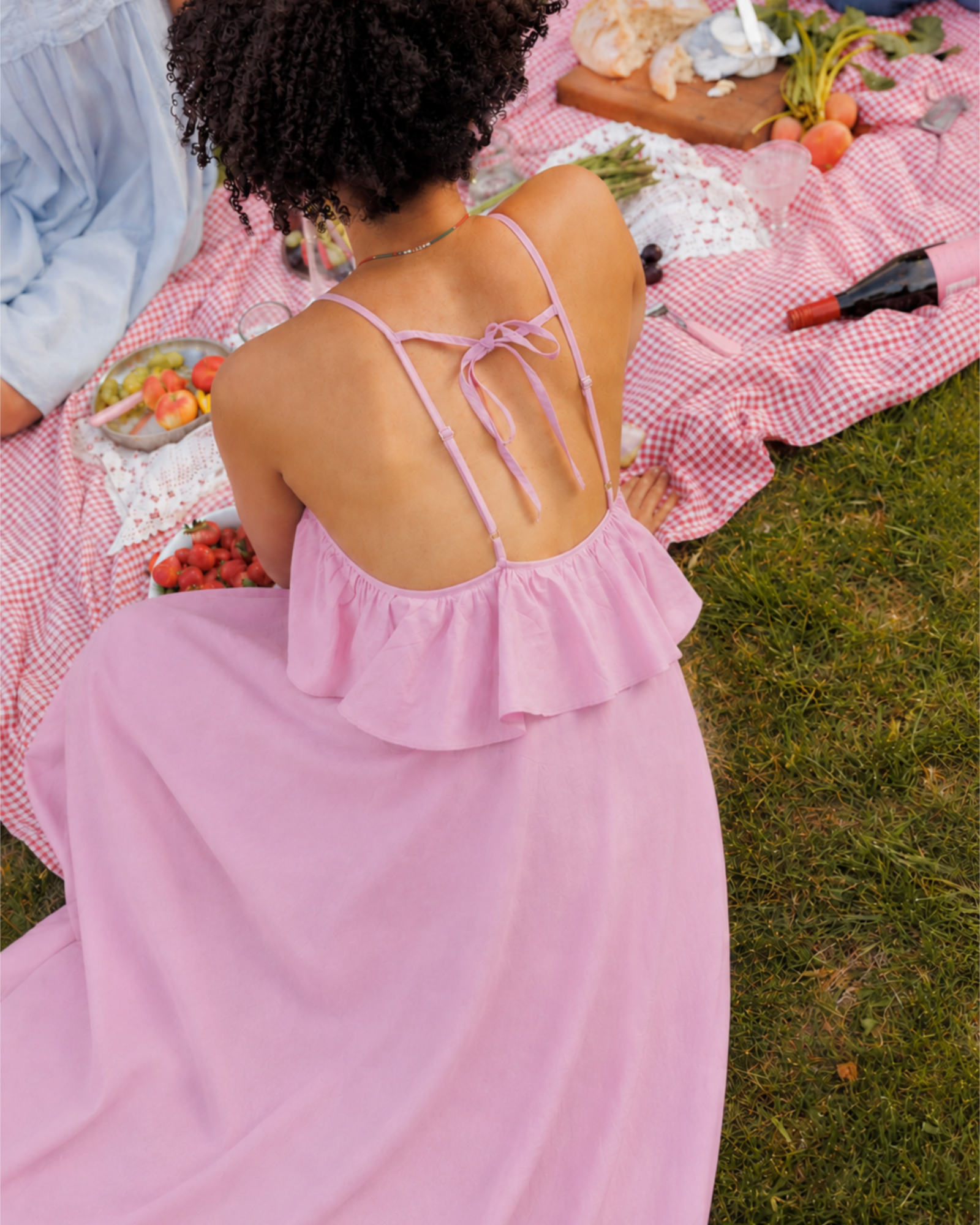 Woman in a pink dress sitting on a checkered blanket with picnic items