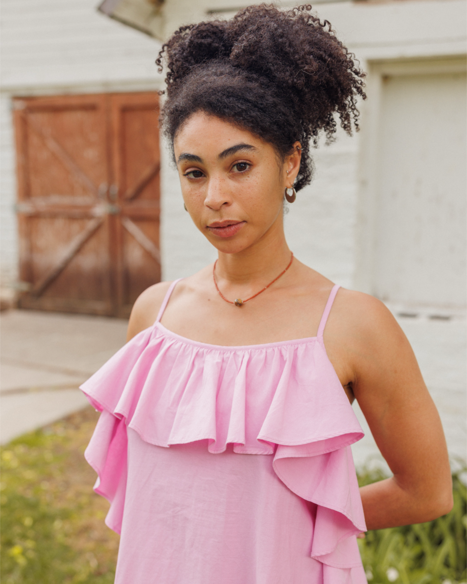 Woman wearing a pink dress with ruffled layers standing outdoors.