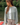 A woman wearing a light gray cropped knit cardigan over a white top and beige plaid pants, standing outdoors near water and trees.