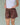 Close-up of a woman wearing a white top and brown shorts on a green background.