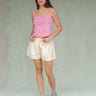 Woman wearing a pink tank top and cream shorts on a green background.