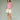 Woman wearing a pink tank top and cream shorts on a green background.