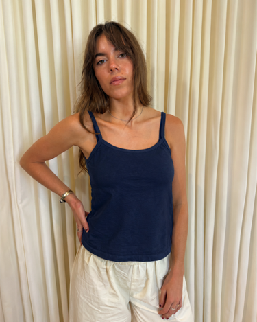 Woman wearing a navy blue tank top and cream pants against a cream curtain background