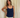 Woman wearing a navy blue tank top and cream pants against a cream curtain background