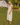 Woman in a yellow dress standing in a grassy field with a white building and trees in the background.