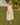Woman in a yellow dress standing in a grassy field with a rustic building in the background