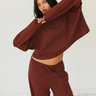 A woman modeling a matching dark red lounge set consisting of a cropped long-sleeve top and wide-leg pants, posed against a clean white studio background.