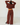 A woman stands with her back to the camera wearing a matching dark red two-piece lounge set consisting of a cropped long-sleeve top and wide-leg pants, set against a plain white wall and light wood floor.