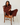 A woman wearing a matching dark red lounge set sits on a wooden chair against a white wall and white floorboards.