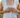 Woman buttoning a white sleeveless top with lace detailing.