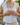 Woman buttoning a white sleeveless top with lace detailing.