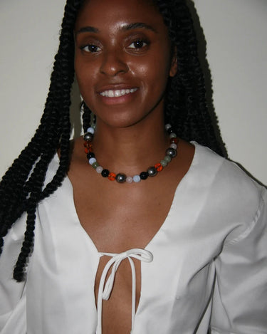 Woman wearing a white blouse with a deep neckline and a colorful necklace against a plain background