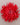 A bright red fabric flower with layered, spiky petals arranged in a round daisy-like shape, photographed from above on a plain light gray background.
