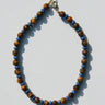 A beaded necklace made of brown tiger's eye beads and small blue spacer beads, with a gold clasp, laid flat on a light gray background.