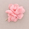 A light pink fabric flower brooch with a gold-tone pin, displayed on a neutral taupe background.